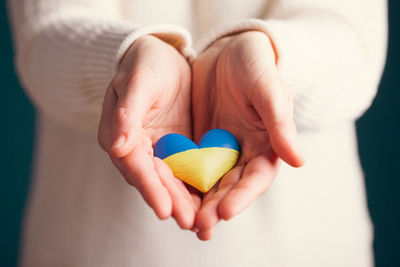 Cropped hand of woman holding heart shape against wall