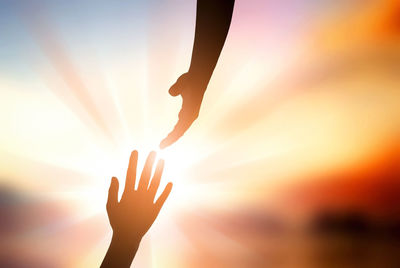 Silhouette hands reaching each other against sky during sunset