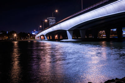 Illuminated bridge over river in city at night
