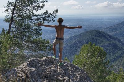 Rear view of woman standing on rock against sky