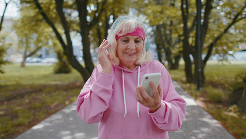 Senior woman using phone while listening music through headphones in park