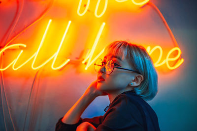 Close-up of thoughtful woman standing against illuminated light