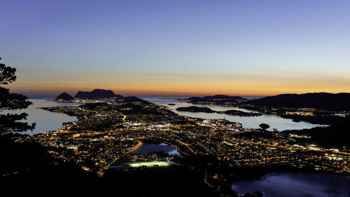 Illuminated city at waterfront during sunset