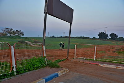 People on field by fence against sky