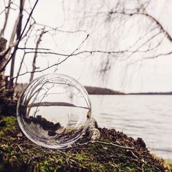 Close-up of crystal ball at lakeshore against sky