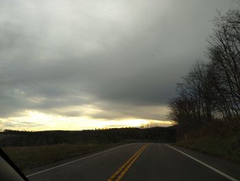 Road by trees against sky during sunset