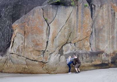 Man assisting woman in climbing on rock formation