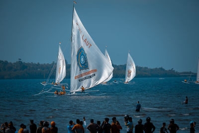 People on sailboat sailing in sea against sky