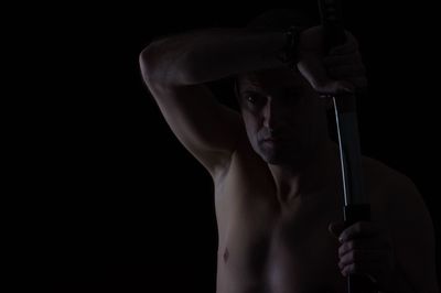 Close-up of shirtless man holding sword against black background