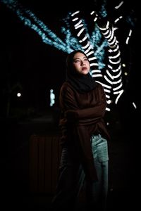 Portrait of beautiful young woman standing in dark room