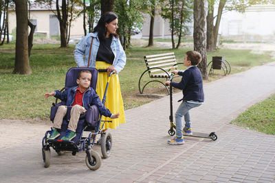 Family with cerebral palsy child on special wheelchair walking outdoors. integration