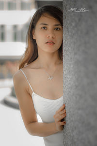 Portrait of young woman standing by wall