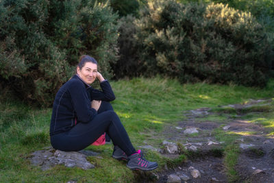 Adult woman sitting on a rock in the forest, hiking in glendalough, wicklow mountains, ireland