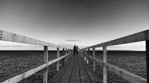 Rear view of people walking on pier over sea against sky