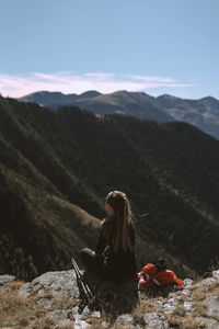 Young woman sitting on mountain against sky