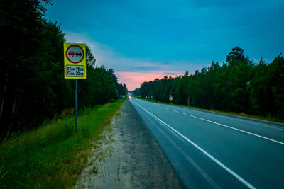 Road sign by trees against sky