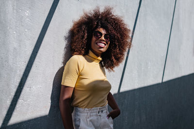 Black woman with afro hair posing in front of a gray wall looking away