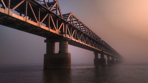 Low angle view of bridge over river against sky during sunset