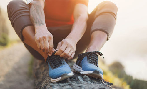 Fit tattoo man tie his sport shoes outdoor during jogging session - focus on hands