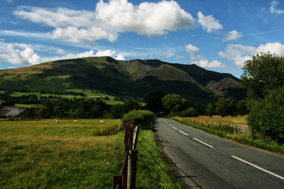 Scenic view of road amidst field in front of mountain against sky in the peak district, england