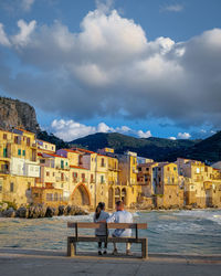 People sitting by buildings against sky in city