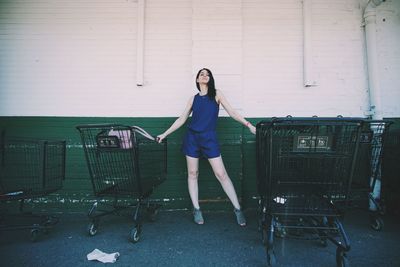 Woman standing amidst shopping carts against wall