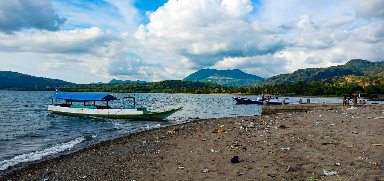 BOATS MOORED ON BEACH AGAINST SKY