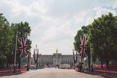 Road leading towards historic building in city against cloudy sky