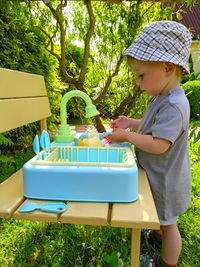 Little boy learns to wash dishes in a toy washbasin on the backyard