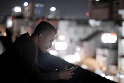 Side view of young man using smart phone at night