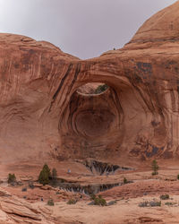 Large natural sandstone arch and rock formations dwarfs the hikers in the extreme terrain