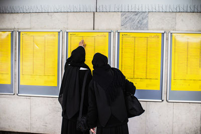 Rear view of people standing against yellow wall