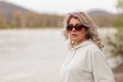 Portrait of young woman wearing sunglasses while standing against lake