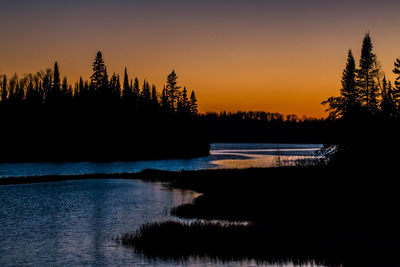 Silhouette trees by lake against sky during sunset