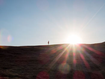 Silhouette person standing on hill against bright sun during sunset
