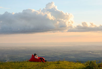 Man sitting on field against sky during sunset