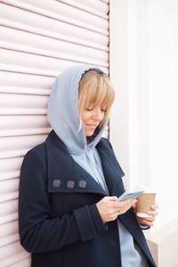 Woman in hood using mobile phone while standing outdoors