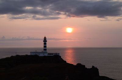 Lighthouse by sea against sky during sunset