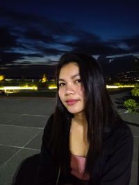 Portrait of a smiling young woman against illuminated sky at night