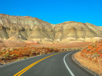 Road leading towards mountains against clear sky