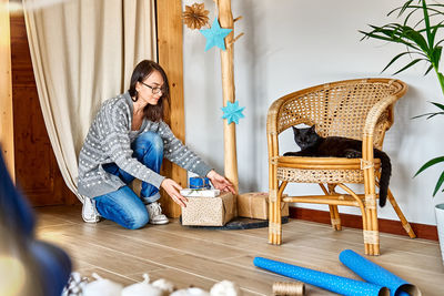 Woman wrapping christmas gifts in craft recycled paper in the room with alternative christmas tree