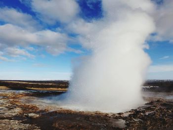 Geyser spraying water against cloudy sky