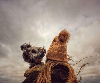 Rear view of woman with dog sitting against sky