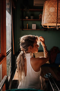 View from the back of a woman sitting in a cafe by the window and collecting her hair in a ponytail