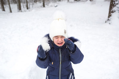 Little girl crying outside in winter. a child in warm clothes is upset, cold, wipes away tears, 