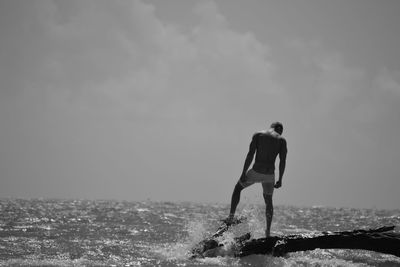 Full length of young man standing at sea shore against sky
