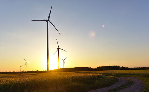 Wind turbines on field against sky during sunset