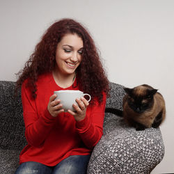 Smiling young woman holding coffee cup while sitting on sofa