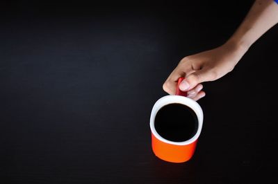 Hand holding coffee cup against black background