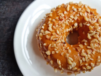 Delicious pastries. donut covered with caramel and nuts on a white plate.